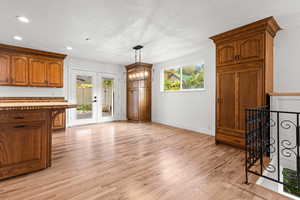 Kitchen with brown cabinetry, light wood-type flooring, a chandelier, french doors, and a textured ceiling