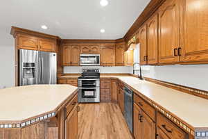 Kitchen featuring brown cabinets, stainless steel appliances, light wood finished floors, light countertops, and recessed lighting