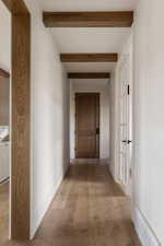 Hallway featuring exposed wood beams, wood-finish flooring, a solid wood door with matte black hardware.