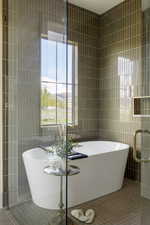 Freestanding soaking tub within a glass-enclosed wet room, featuring floor-to-ceiling vertical subway tile