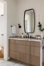 Custom fluted wood-finish vanity with a stone countertop, featuring a black framed mirror and wall sconces