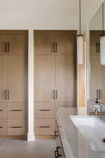 Integrated wood-finish cabinetry with matte black hardware, featuring ample storage, a built-in vanity with an undermount sink, and a stone countertop