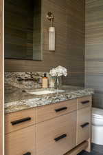 Main level powder room/half bath with custom vanity with light wood-finish cabinetry and matte black hardware, featuring a stone countertop with an undermount sink and wall-mounted faucet