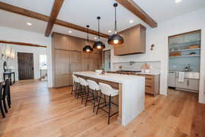 Kitchen with a large island, cabinet finished double fridge/freezer, beamed ceiling, stone counters with waterfall edges, and modern light fixtures