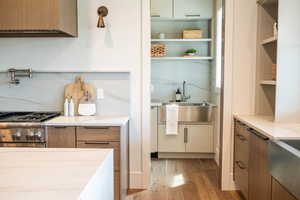 Two tone kitchen with light stone counters, light wood finished floors, stainless steel stove, two tone cabinetry, and modern cabinets