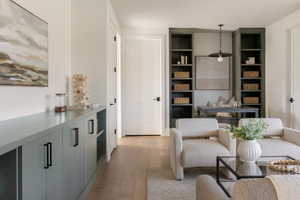 Expansive living area featuring light wood-finish flooring, a long built-in cabinet with dark hardware, and recessed shelving on either side of a central desk area