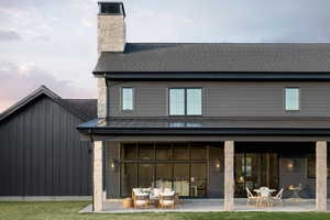 Rear exterior featuring a covered patio, stone columns, dark siding, multiple windows, and a prominent stone chimney