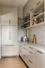 Butlers pantry with integrated refrigerator-freezer unit with custom paneling, extensive lower cabinetry with contemporary hardware, open shelving, and a veined countertop and backsplash