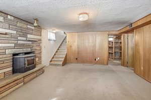 Finished basement featuring a wood stove, stairs, wooden walls, and carpet floors