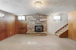 Below grade area with a wood stove, wood walls, healthy amount of natural light, carpet flooring, and stairway