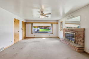 Unfurnished living room featuring a stone fireplace, carpet flooring, and a ceiling fan