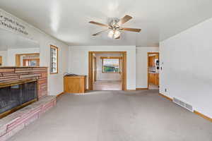 Unfurnished living room with light colored carpet, a stone fireplace, and a ceiling fan