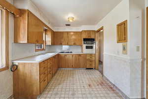 Kitchen featuring brown cabinetry, light countertops, light floors, oven, and black gas cooktop