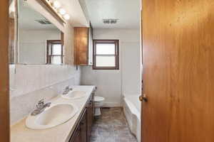 Bathroom featuring a textured ceiling, double vanity, and shower / washtub combination