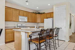 Kitchen featuring light tile patterned flooring, an island with sink, white appliances, a breakfast bar area, and recessed lighting