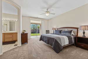 Bedroom featuring access to outside, light colored carpet, a textured ceiling, a ceiling fan, and connected bathroom