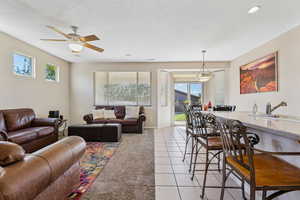 Living area featuring light tile patterned floors, healthy amount of natural light, a textured ceiling, and a ceiling fan