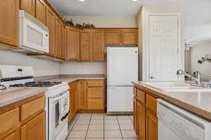 Kitchen featuring white appliances, light tile patterned floors, brown cabinetry, and ceiling fan