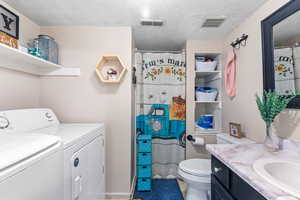 Full bath with a textured ceiling, vanity, washer and dryer, and a shower with shower curtain