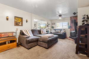 Living area with a wood stove, light colored carpet, a textured ceiling, and a ceiling fan