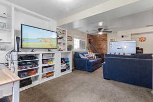 Living area with a wood stove, light colored carpet, a textured ceiling, ceiling fan, and built in shelves