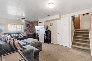 Carpeted living room featuring a wood stove, a textured ceiling, stairway, and a ceiling fan