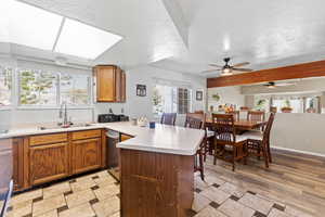 Kitchen featuring a peninsula, light countertops, brown cabinetry, a breakfast bar, and stainless steel dishwasher