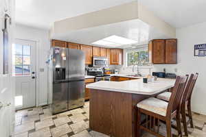 Kitchen featuring appliances with stainless steel finishes, light countertops, a peninsula, a breakfast bar, and brown cabinets