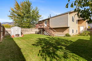Rear view of house with a fenced backyard, stairway, and a storage unit