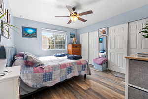 Bedroom with two closets, wood finished floors, and a ceiling fan