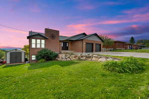 View of front of property with board and batten siding, concrete driveway, a yard, brick siding, and a storage shed
