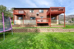Back of house with a trampoline, a lawn, brick siding, a balcony, and a deck with mountain view