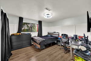 Bedroom with light wood finished floors, a textured ceiling, a decorative wall, and a desk