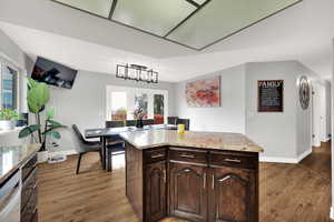 Kitchen featuring dark brown cabinetry, dark wood-style floors, a kitchen island, and light stone counters