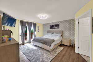 Bedroom featuring access to exterior, wood finished floors, and wallpapered walls