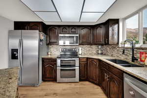 Kitchen with dark brown cabinets, appliances with stainless steel finishes, light stone counters, and light wood-type flooring