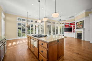 Kitchen with light stone counters, pendant lighting, light wood-style floors, a kitchen island, and a tiled fireplace