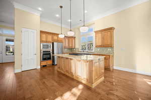 Kitchen featuring light stone countertops, appliances with stainless steel finishes, dark wood-style flooring, crown molding, and decorative backsplash