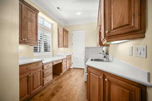 Kitchen with built in desk, ornamental molding, brown cabinets, light countertops, and light wood-style floors