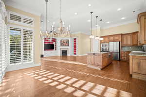 Kitchen with light stone counters, a fireplace, crown molding, pendant lighting, and light wood finished floors
