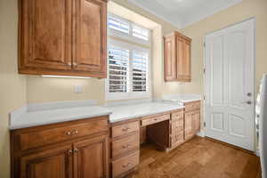 Office area featuring built in desk, crown molding, wood finished floors, and washer / dryer
