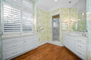 Bathroom with crown molding, a chandelier, dark wood-style floors, wallpapered walls, and two vanities
