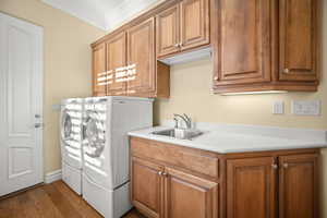 Washroom featuring crown molding, wood finished floors, cabinet space, and independent washer and dryer