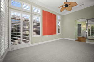 Unfurnished room with ornamental molding, arched walkways, carpet flooring, and ceiling fan