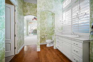 Half bath featuring wallpapered walls, crown molding, dark wood-type flooring, vanity, and ceiling fan