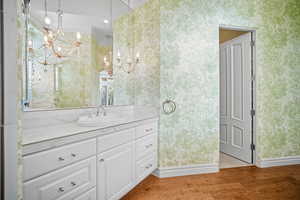 Bathroom with light wood-style flooring, vanity, wallpapered walls, and a chandelier
