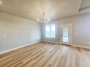 Unfurnished dining area featuring a textured ceiling, light wood finished floors, and a chandelier