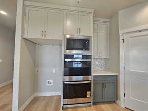 Kitchen with stainless steel appliances, gray cabinetry, light wood-style flooring, decorative backsplash, and a textured ceiling