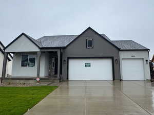 View of front of home with a shingled roof, a front lawn, concrete driveway, covered porch, and stucco siding