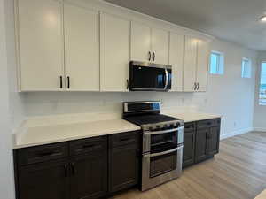 Kitchen featuring stainless steel appliances, white cabinetry, light wood-style flooring, dark cabinetry, and light stone countertops